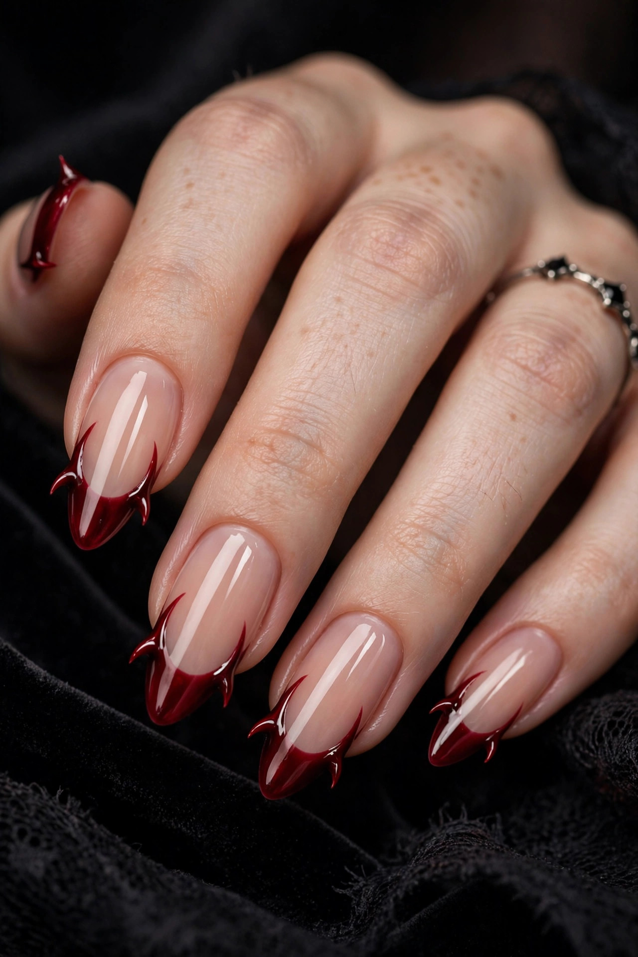Nude nails with deep red French tips extended into tiny horn-like flicks